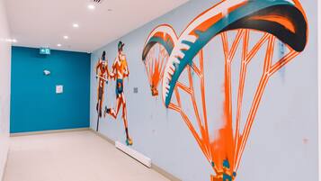 Un pasillo con un mural de una persona en paracaídas, una pared azul y un suelo blanco.