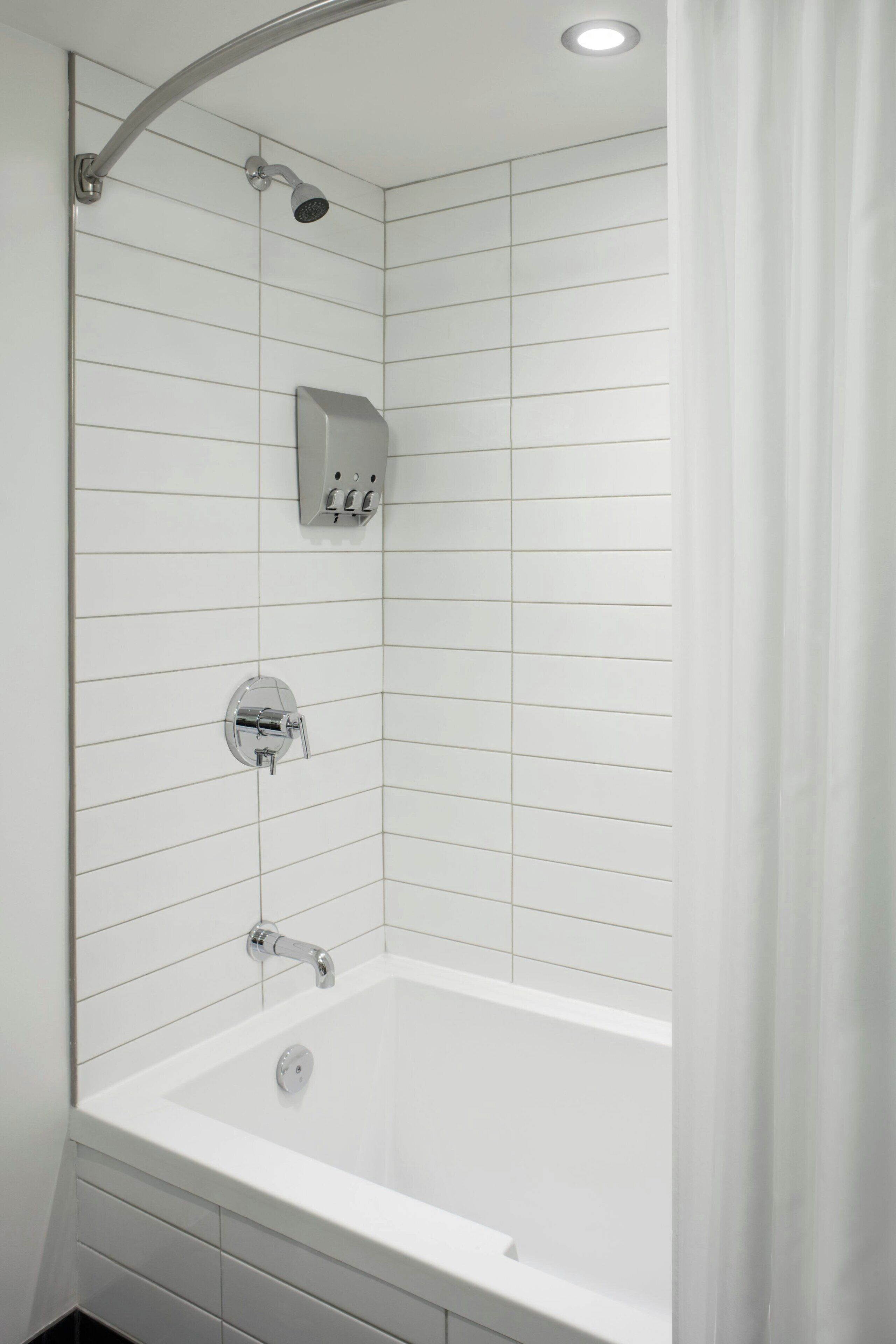 Un baño moderno con ducha de azulejos blancos, inodoro empotrado y bañera.
