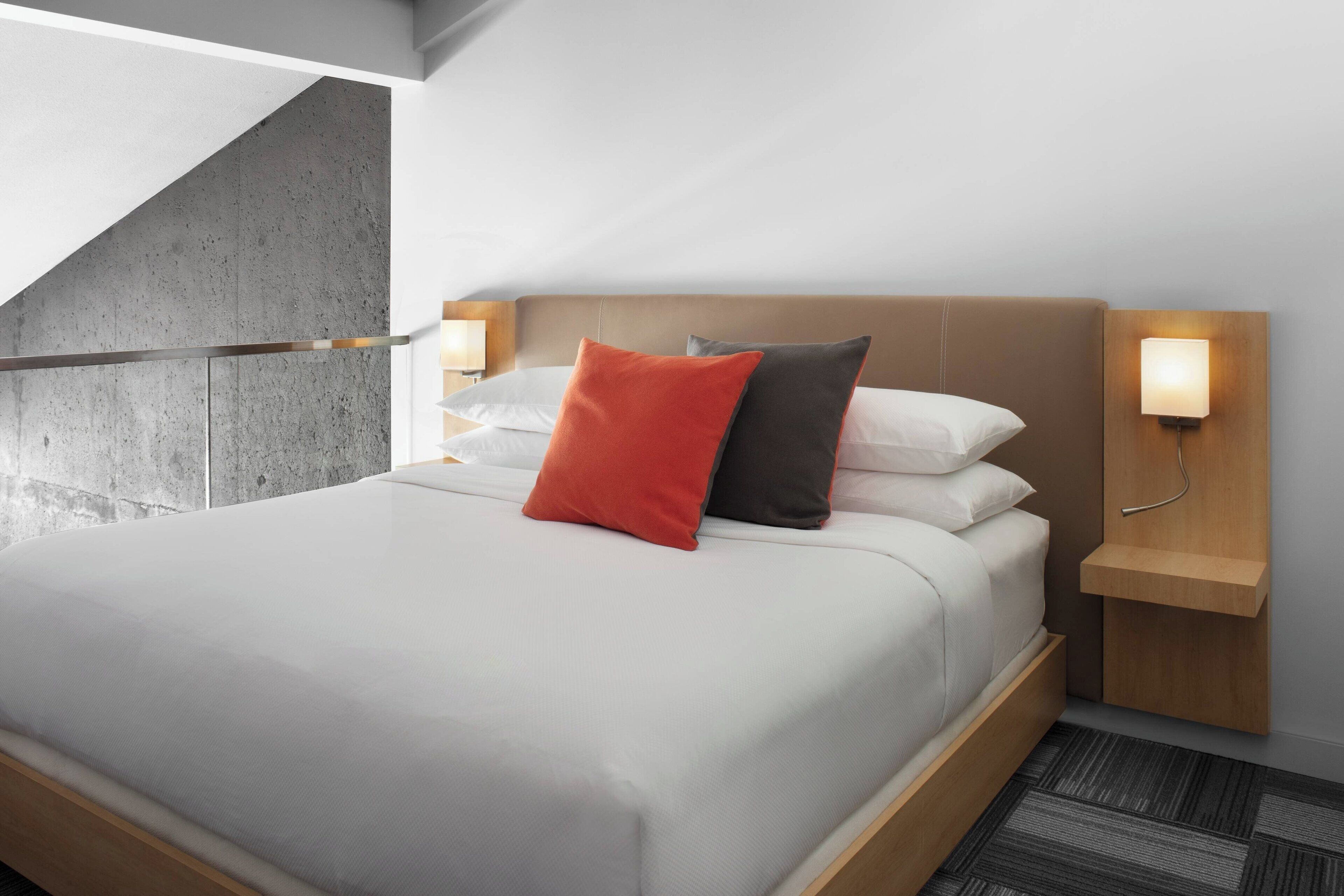 Een moderne hotelkamer met een groot bed, een houten hoofdbord en twee nachtkastjes met wandlampen.
