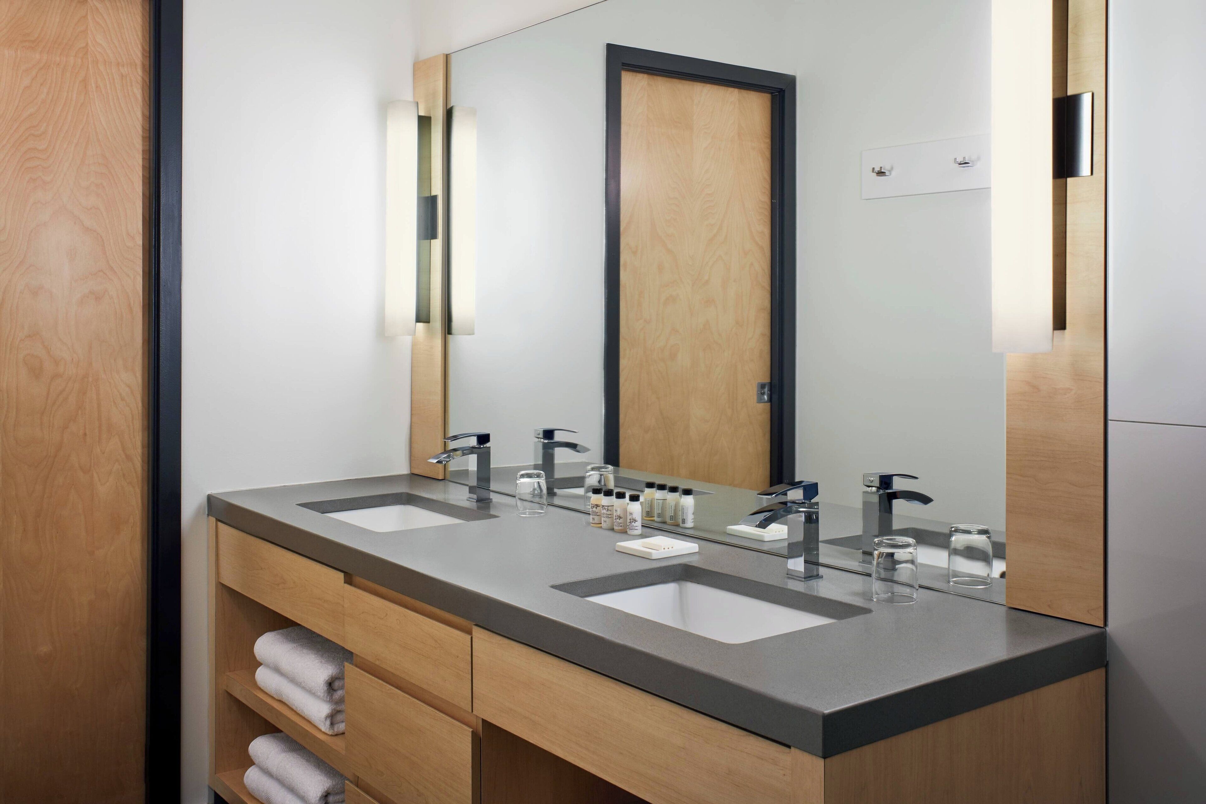 A modern bathroom with two sinks, a large mirror, and wooden cabinetry.