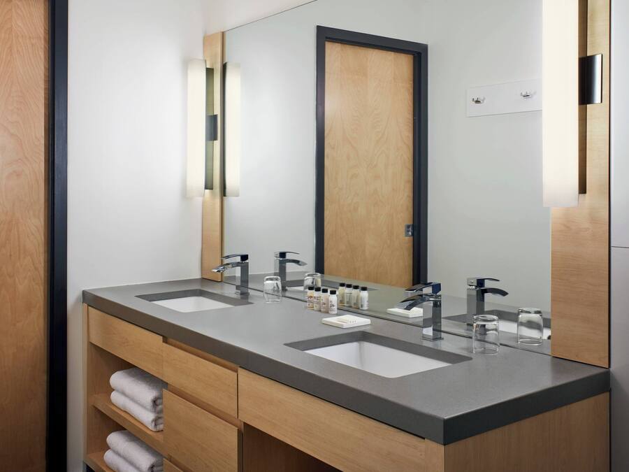 A modern bathroom with two sinks, a large mirror, and wooden cabinetry.