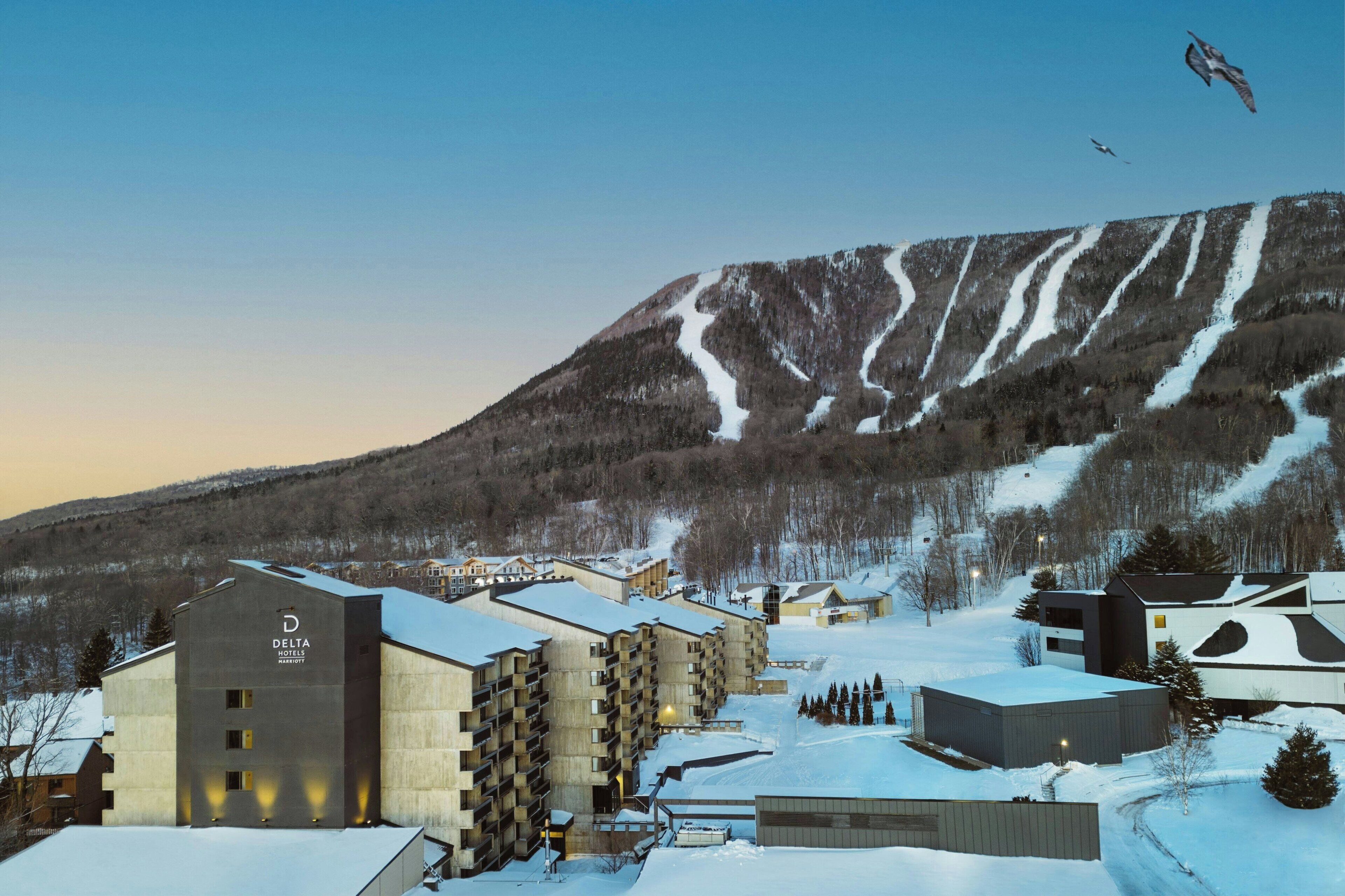 A hotel with multiple buildings, a ski slope in the background, and a clear sky.