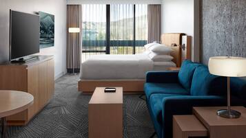 Una habitación de hotel con cama, televisión, sofá, escritorio y ventana con cortinas.