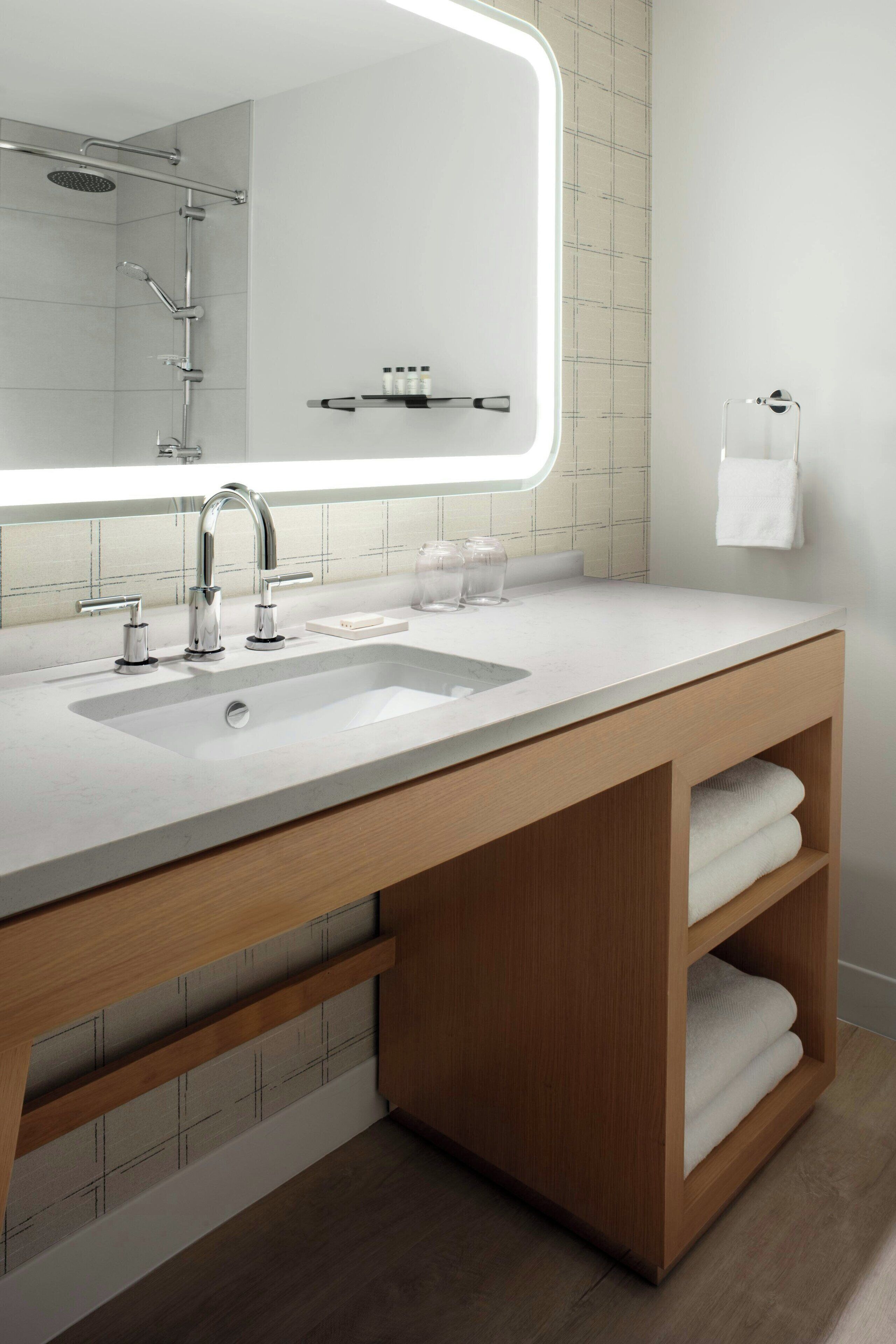 A modern bathroom with a large mirror, a white sink, and wooden cabinetry.