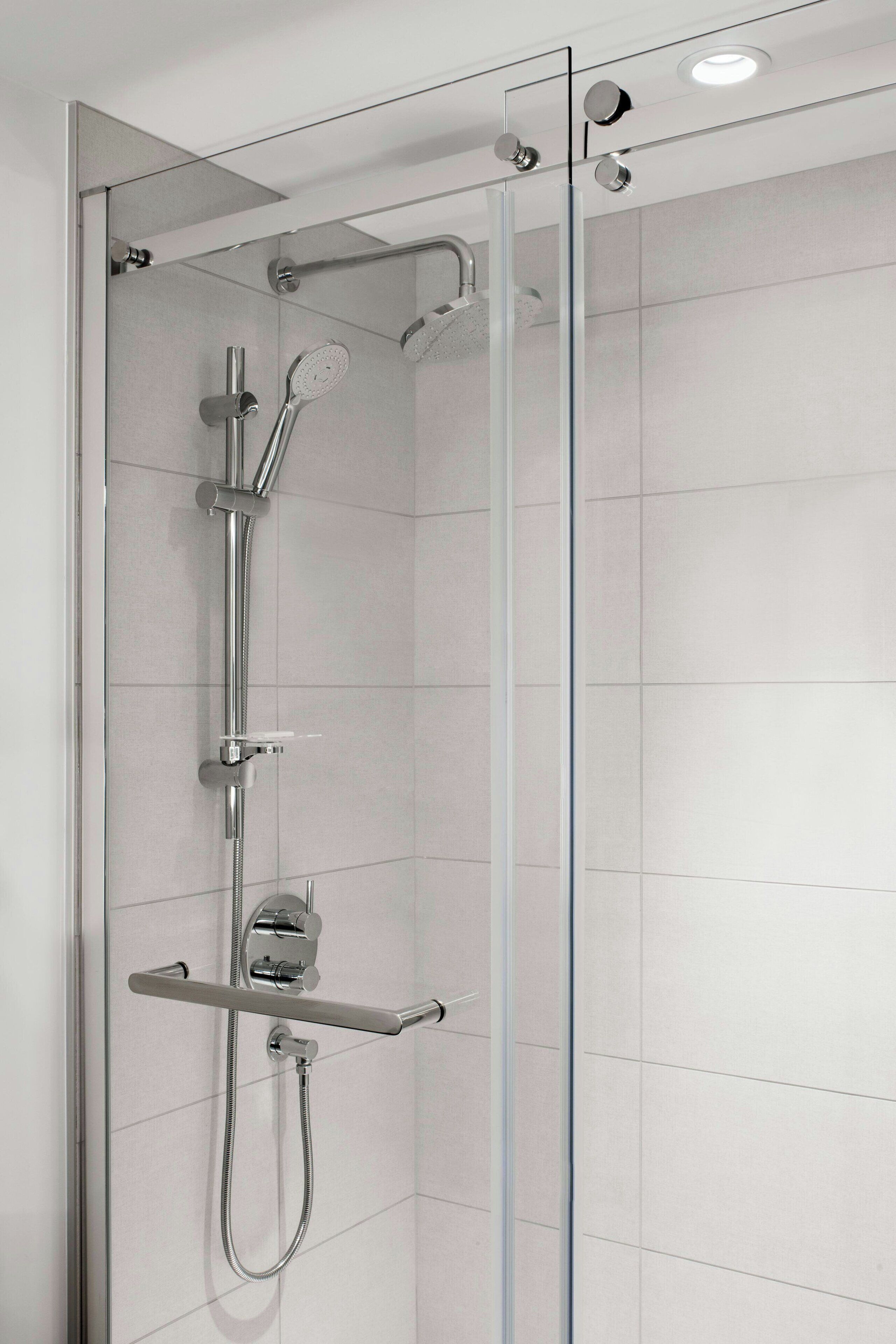 Eine moderne Dusche mit Glasabtrennung, Chromarmaturen und Bedienfeld.