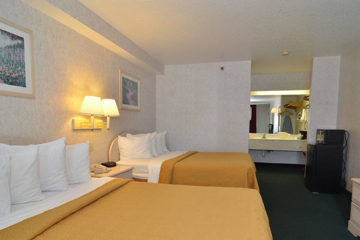 Une chambre d’hôtel avec deux lits, un bureau, une lampe, un réfrigérateur et un miroir.