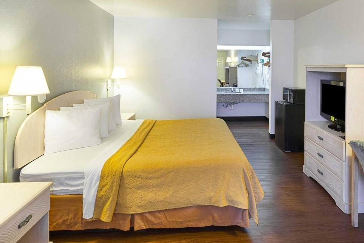 Une chambre d’hôtel avec un lit, des lampes de chevet, une télévision, une commode et, au fond, une petite cuisine.
