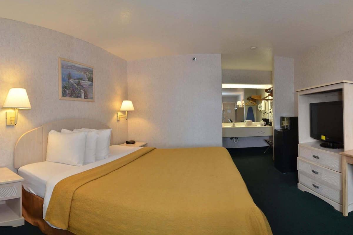 Une chambre d’hôtel avec un lit, des lampes de chevet, une télévision, un bureau et une salle de bain visible au fond.