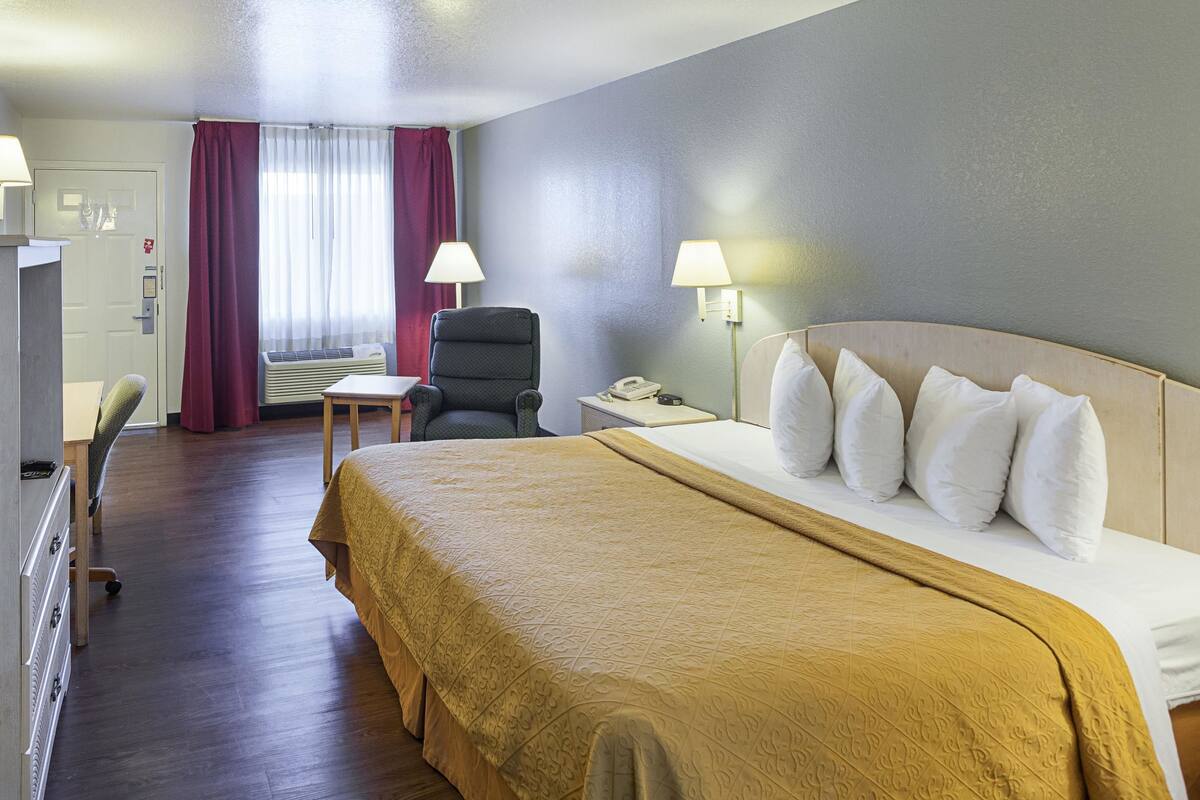 Une chambre d’hôtel avec un grand lit, un bureau avec une lampe, une chaise et une armoire.