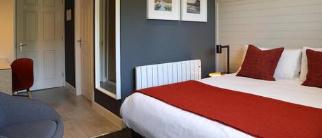 A hotel room with a bed, a red chair, a white radiator, and two framed pictures on the wall.