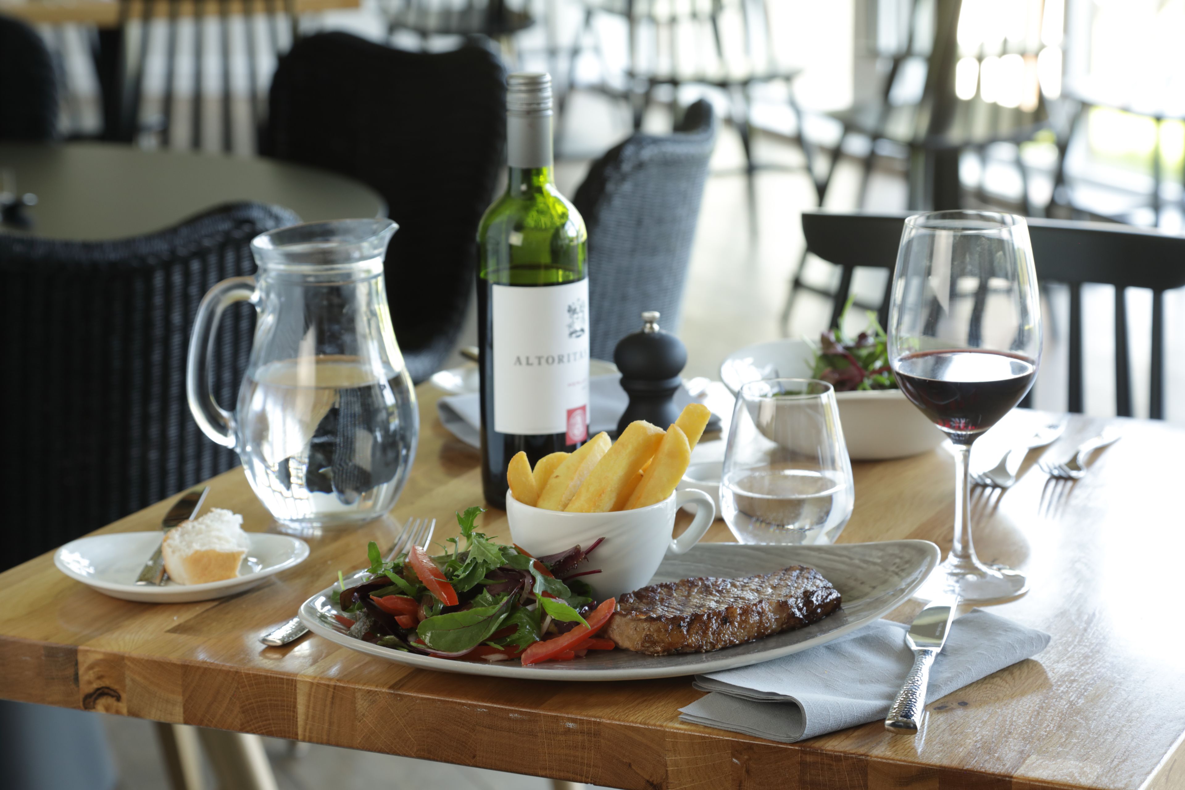 Une table dressée pour le dîner, avec un steak, des frites, une salade et une bouteille de vin.