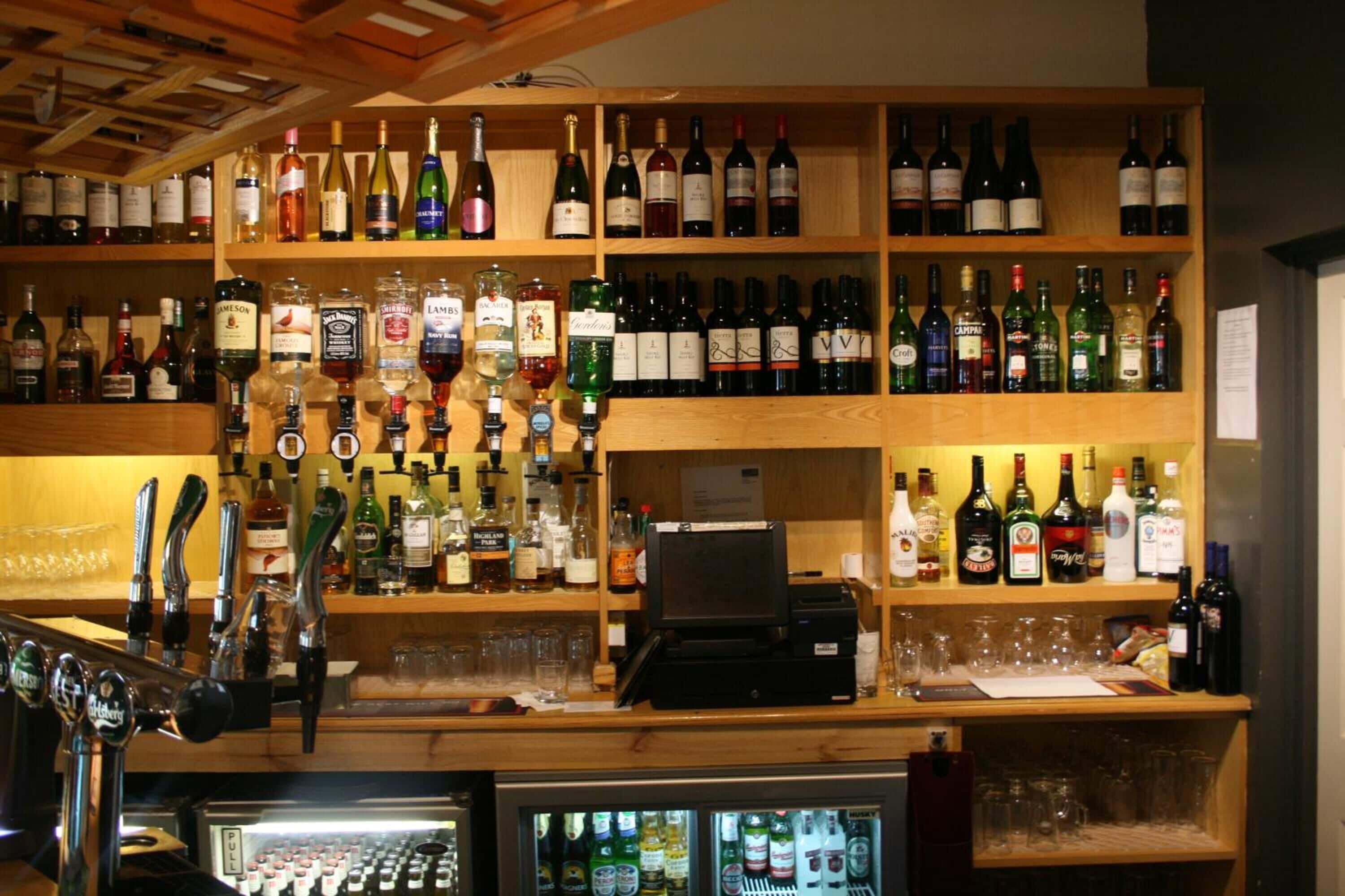 A bar area with multiple shelves of liquor bottles, a cash register, and a refrigerated display case.