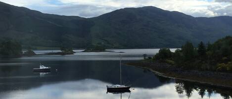 A calm lake with boats, surrounded by mountains and a cloudy sky.