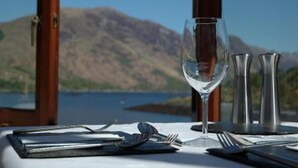 Mesa posta com taça de vinho, talheres e saleiro e pimenteiro, com vista para uma montanha e um lago.