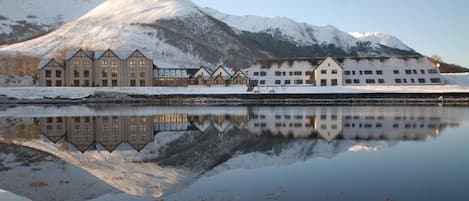 Un hotel con varias construcciones reflejadas en aguas tranquilas, rodeado de montañas nevadas.