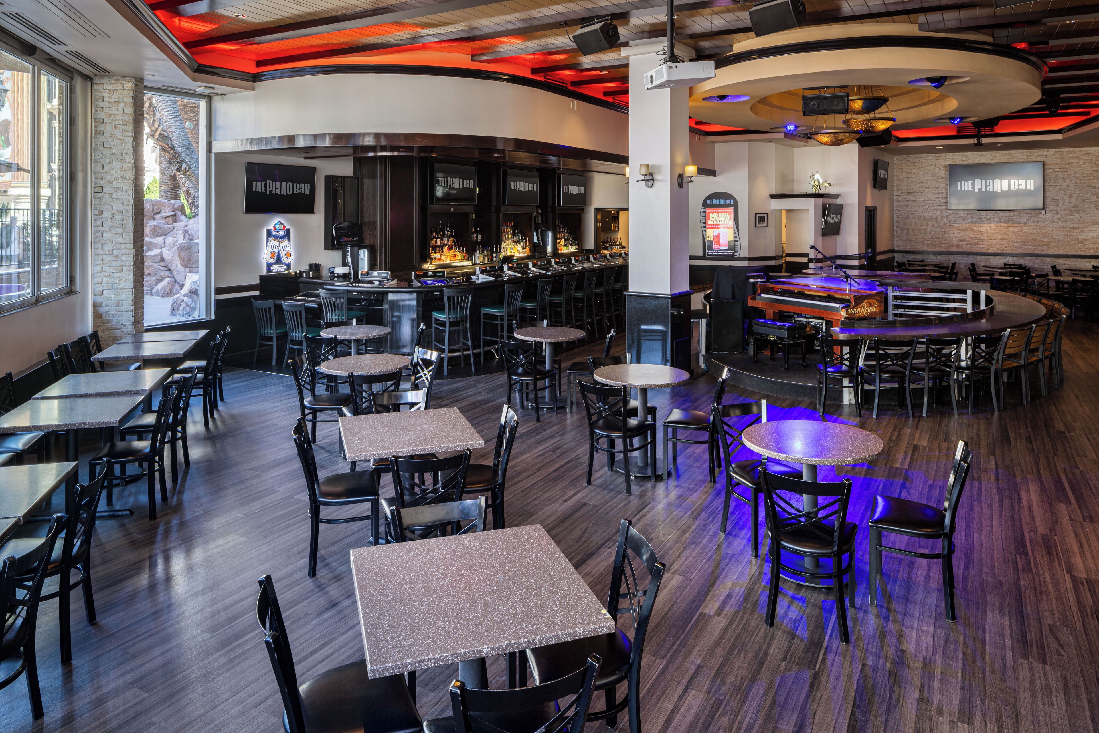 Un restaurante con varias mesas y sillas, una zona de bar y un piano.