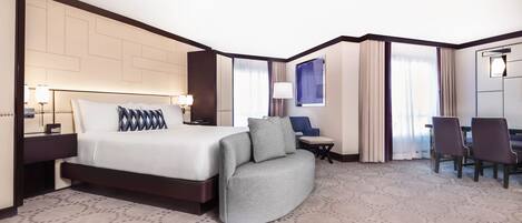 A hotel room with a large bed, a sofa, a desk, and a dining area.