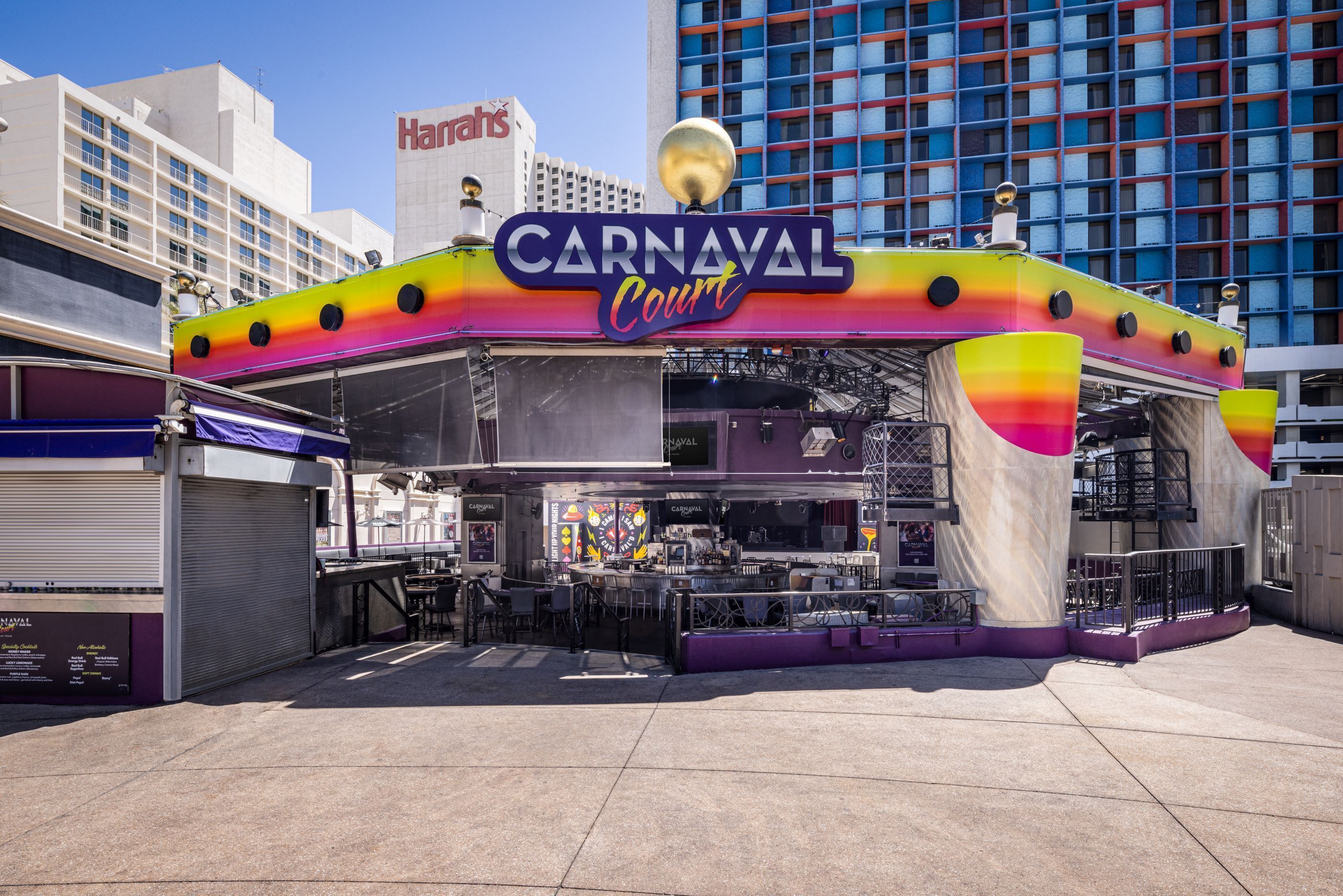 Un espace de restauration animé, sur le thème du carnaval, avec une enseigne colorée, et entouré d’un environnement urbain moderne.