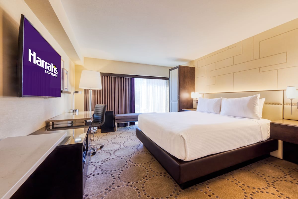 A hotel room with a large bed, a desk, a chair, a lamp, and a Harrah's Las Vegas sign on the wall.