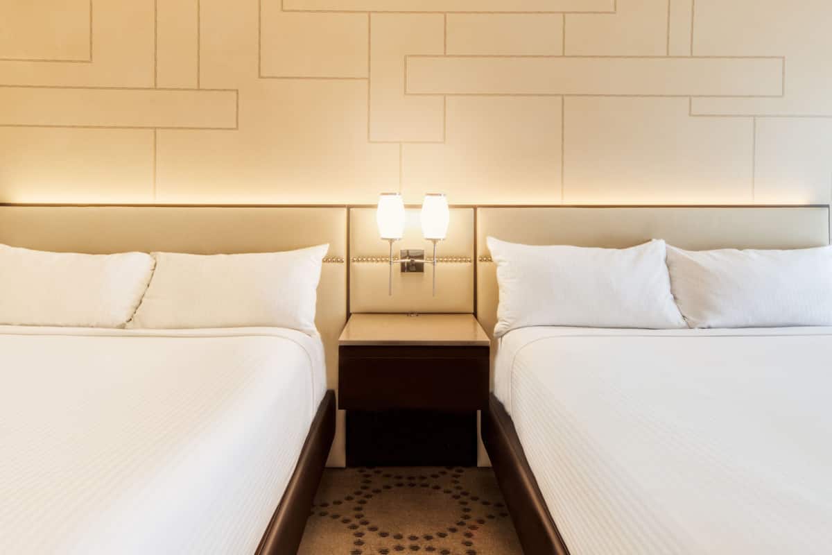 A hotel room with two beds, a nightstand with a lamp, and a patterned carpet.