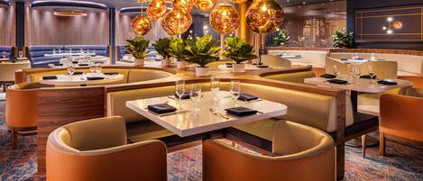 A modern restaurant with round tables, cushioned booths, and hanging spherical lights.