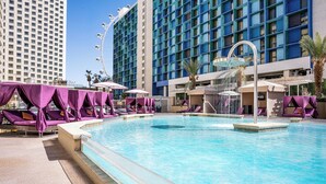 A hotel pool area with a large pool, sun loungers, and a Ferris wheel in the background.