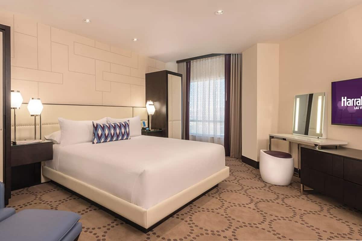 A modern hotel room with a large bed, a desk, a chair, a TV, and a bathroom area.