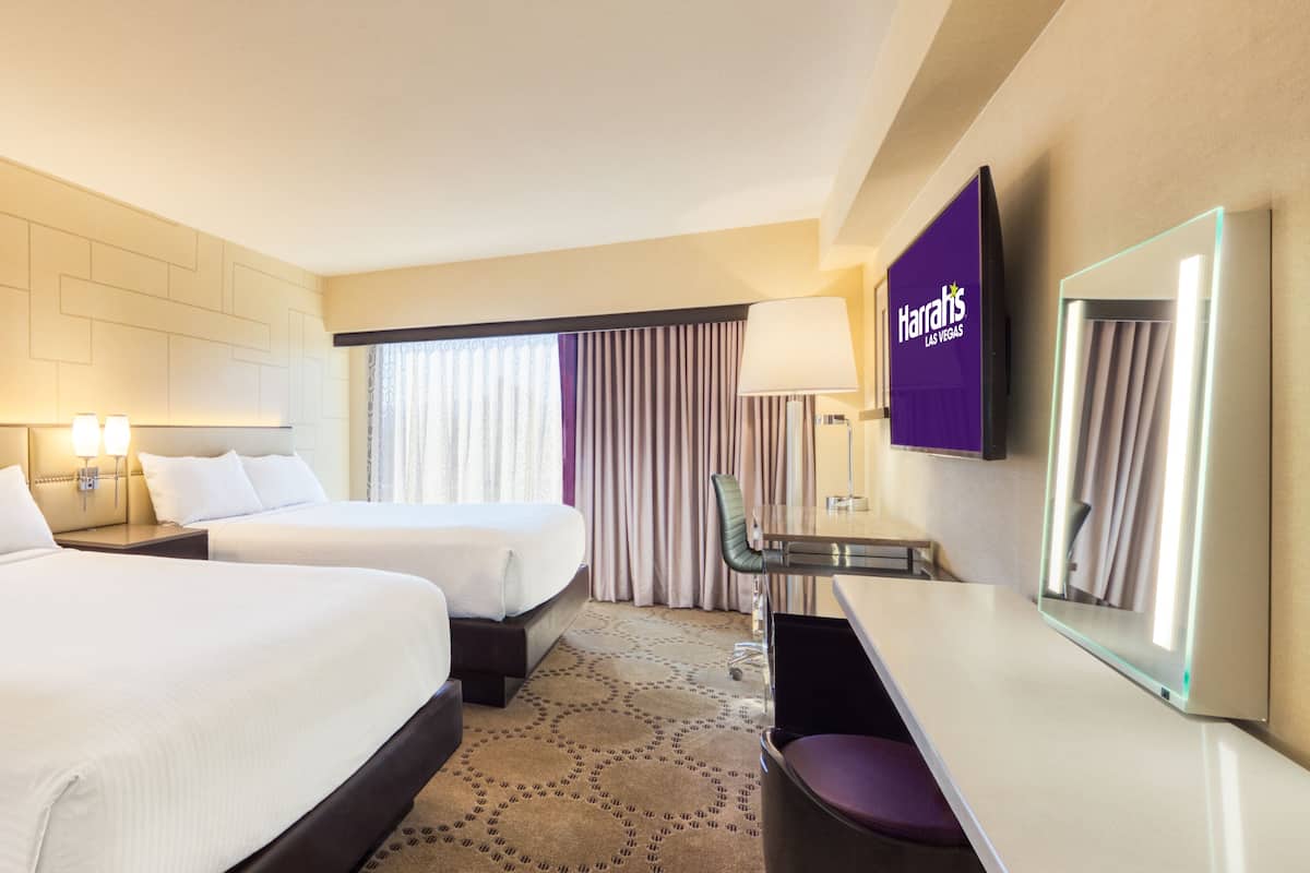 A hotel room with two beds, a desk, a chair, a lamp, and a TV screen displaying 'Harriss Las Vegas'.