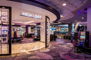 A modern hotel room with a curved sofa, a small round table, and a flat-screen TV mounted on the wall. at Harrah