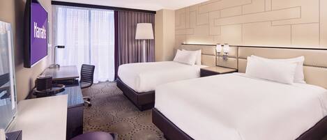 A hotel room with two beds, a desk, a chair, a TV, and a large window with curtains.