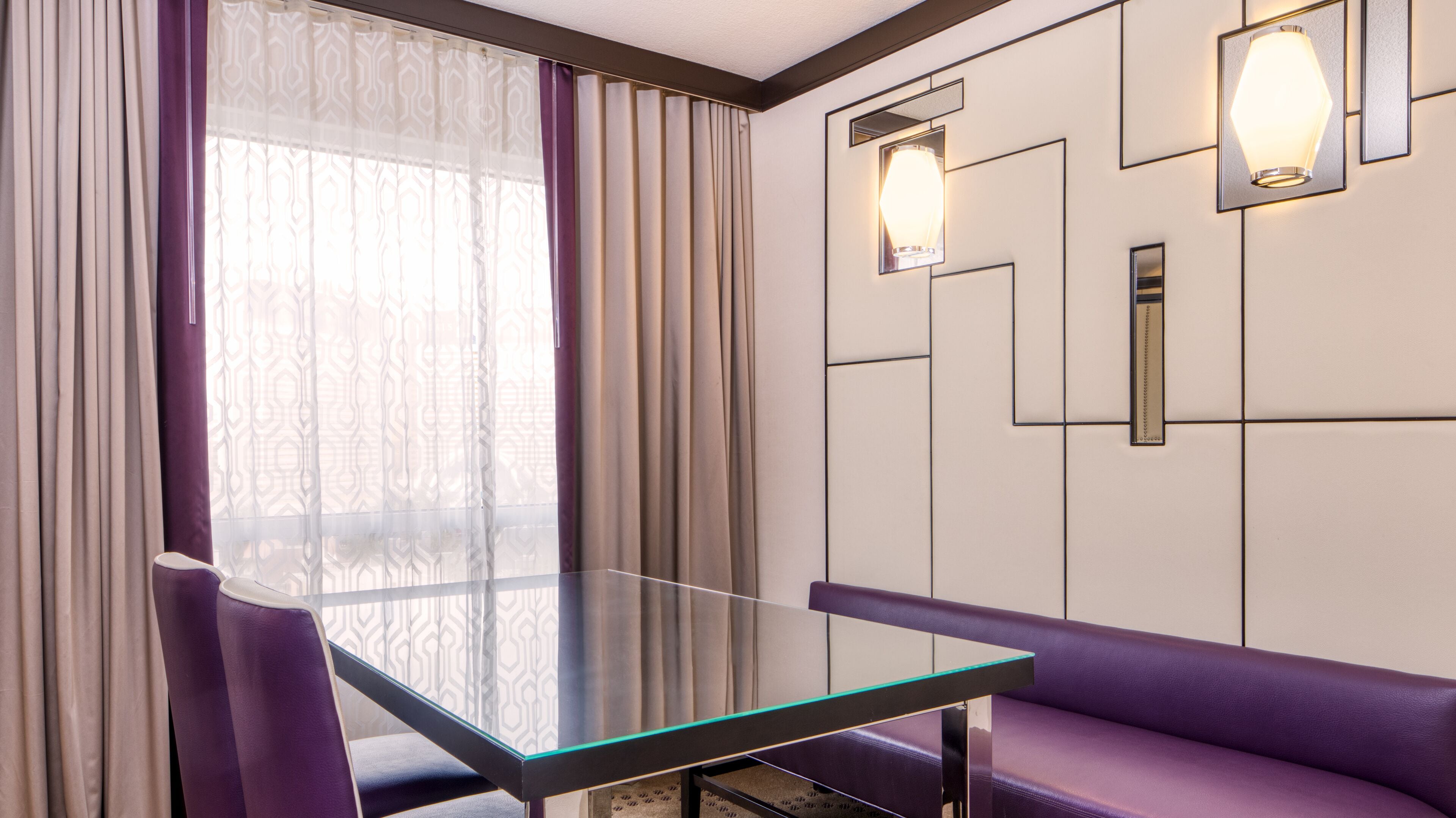 Une pièce moderne avec une table en verre, des sièges violets et des rideaux à motifs.