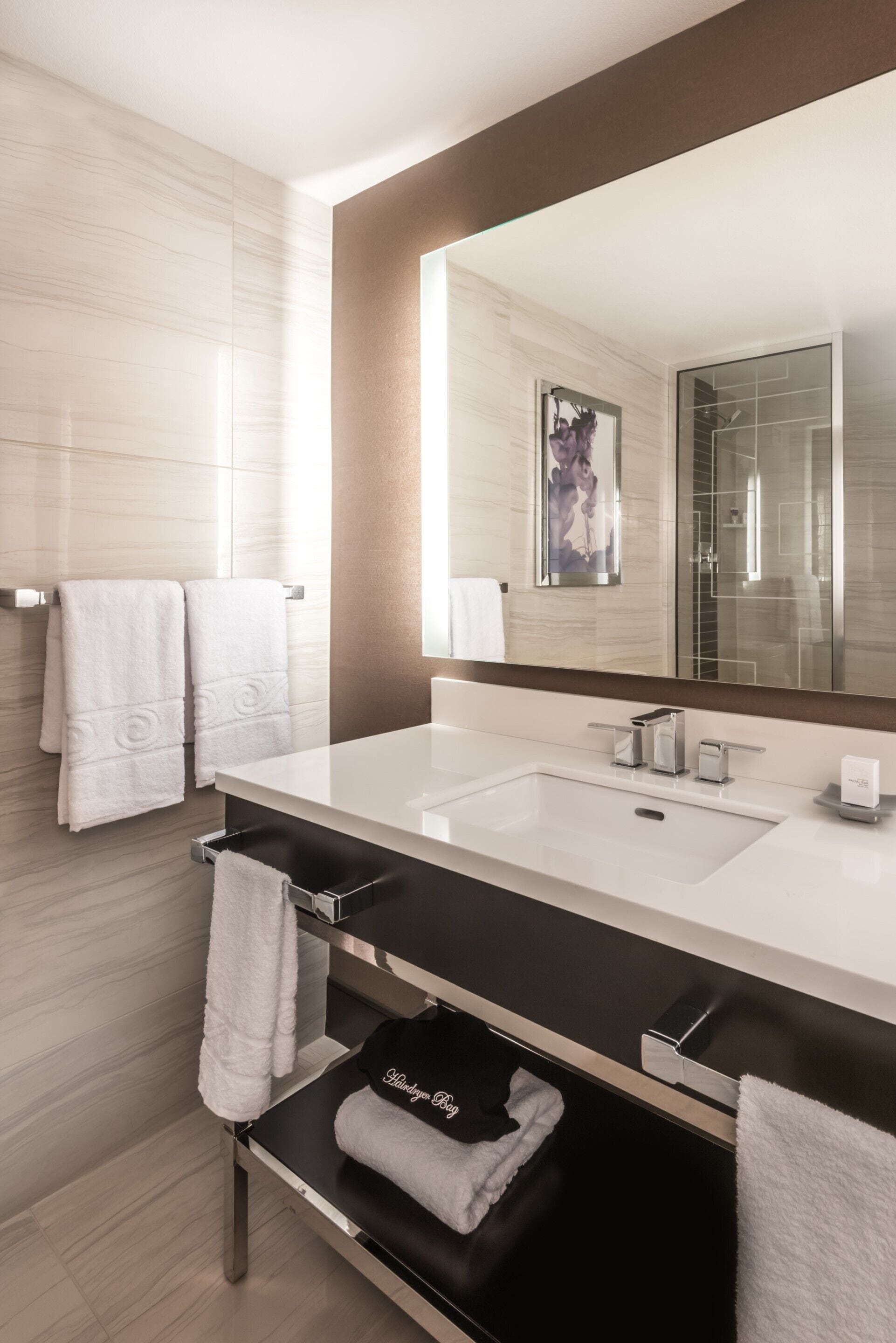 A modern bathroom with a large mirror, white sink, and towel rack.