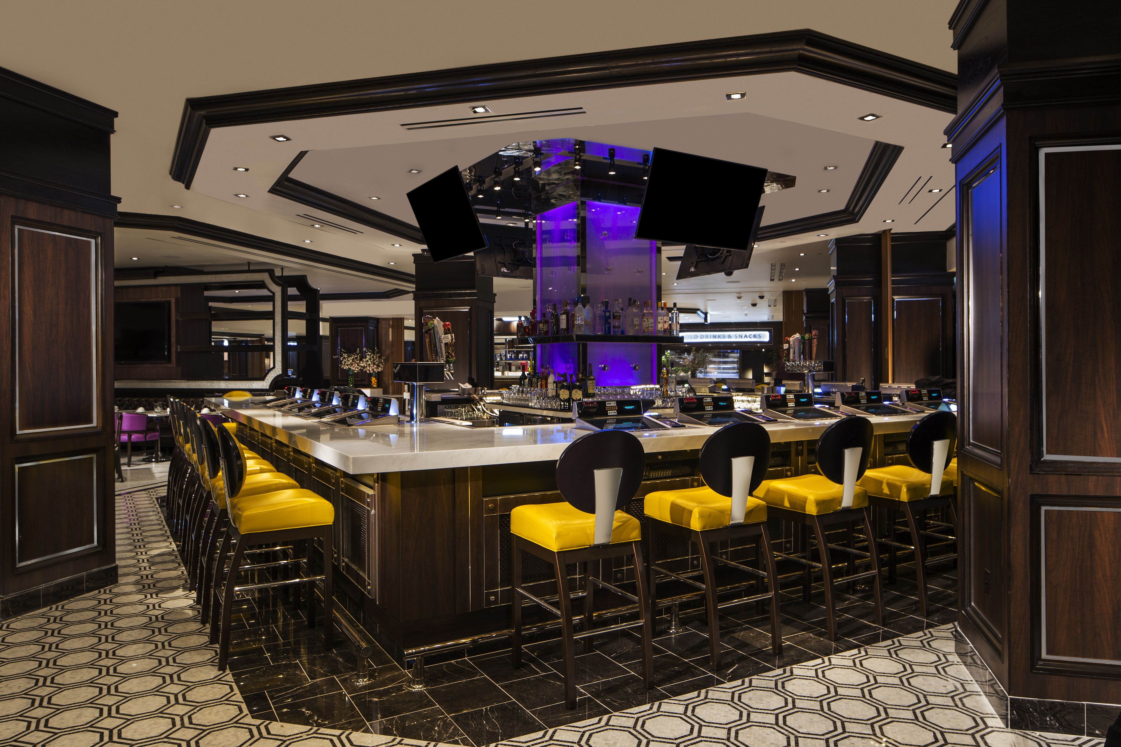 A bar area with a central island, multiple bar stools, and a patterned floor.