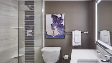 A modern bathroom with a glass shower enclosure, a white toilet, a sink with a mirror, and a wall-mounted towel rack.