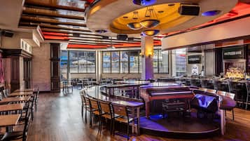A spacious restaurant with a central bar area, multiple dining tables, and a piano.