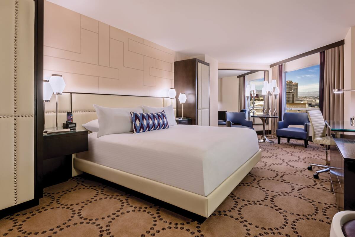 A hotel room with a large bed, a desk, a chair, and a view of the city.