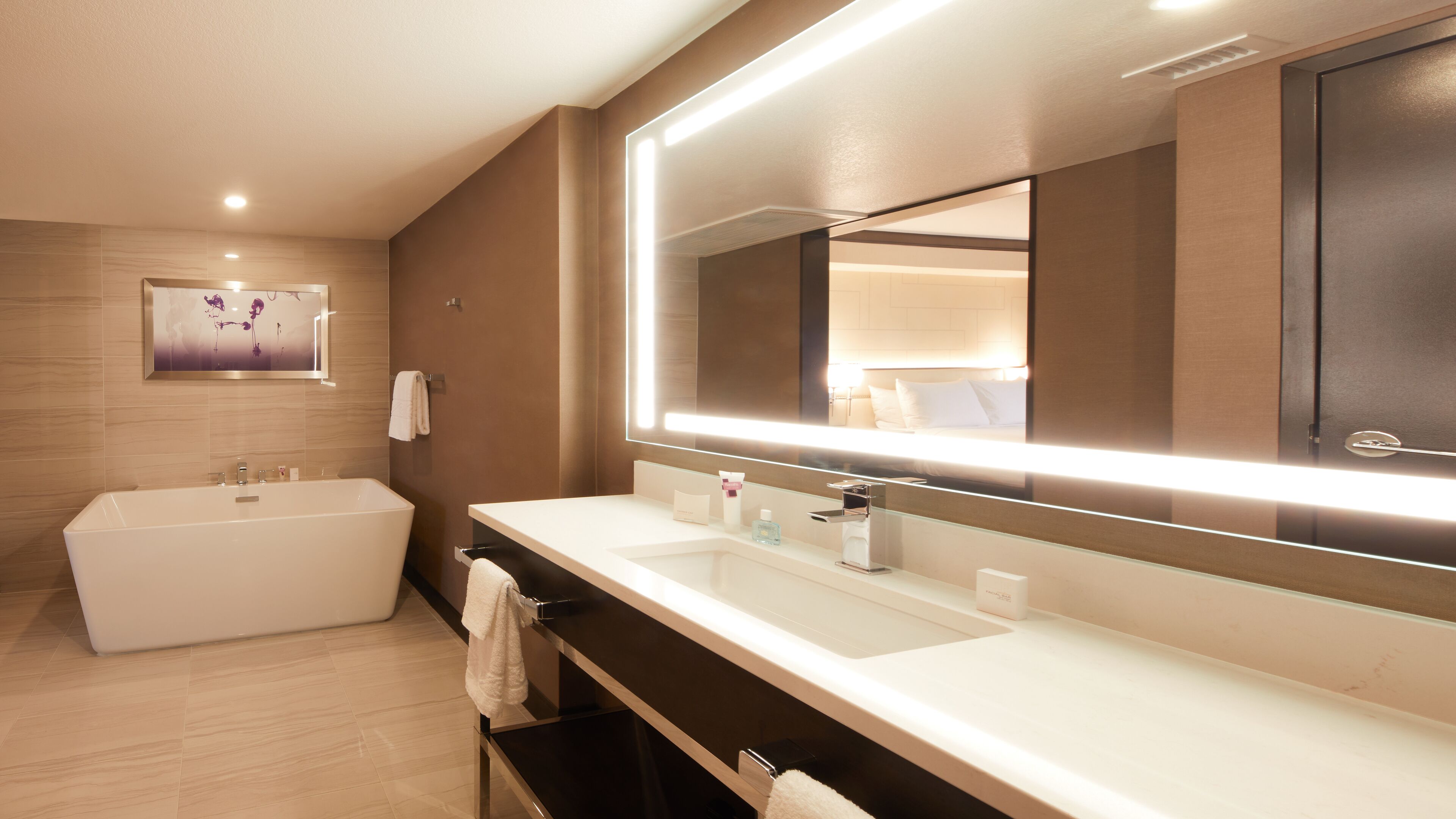 A modern bathroom with a large bathtub, a double sink vanity, and a large mirror with integrated lighting.