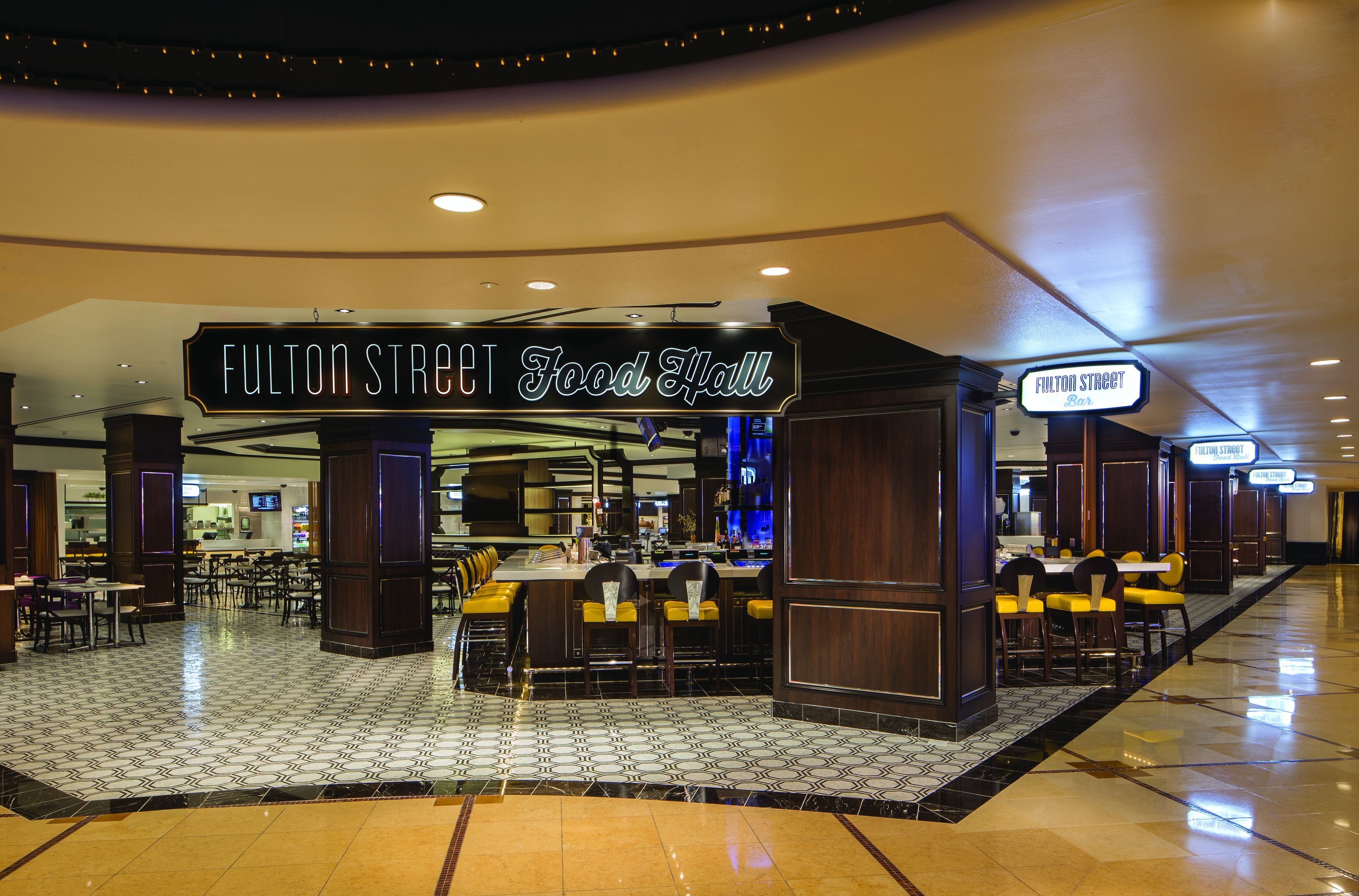 Un restaurant anomenat 'Fulton Street Food Hall' amb una zona de bar, zones d'asseuament i un sòl de rajoles.