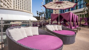 A rooftop lounge area with wicker chairs and purple cushions, overlooking a pool and a high-rise building. - Harrah’s Las Vegas – A Caesars Rewards Destination (Las Vegas)