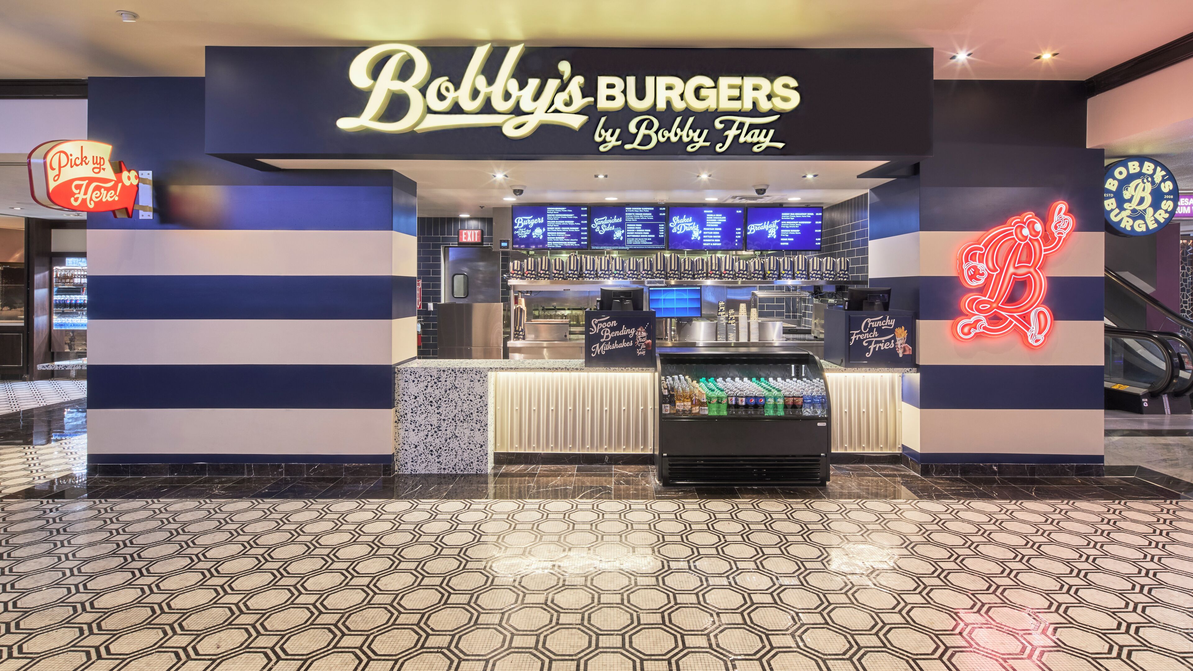 Ein Restaurant namens 'Bobby's Burgers by Bobby Flay' mit einer Neonreklame, einem Kühlvitrine und einer digitalen Speisekarte.