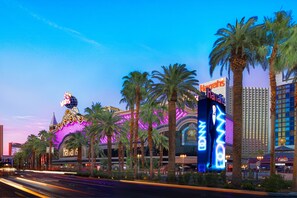 A brightly lit hotel with palm trees and neon signs. - Harrah’s Las Vegas – A Caesars Rewards Destination (Las Vegas)