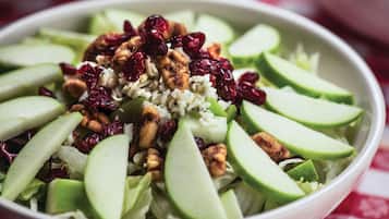A bowl of salad with sliced apples, nuts, and cranberries.