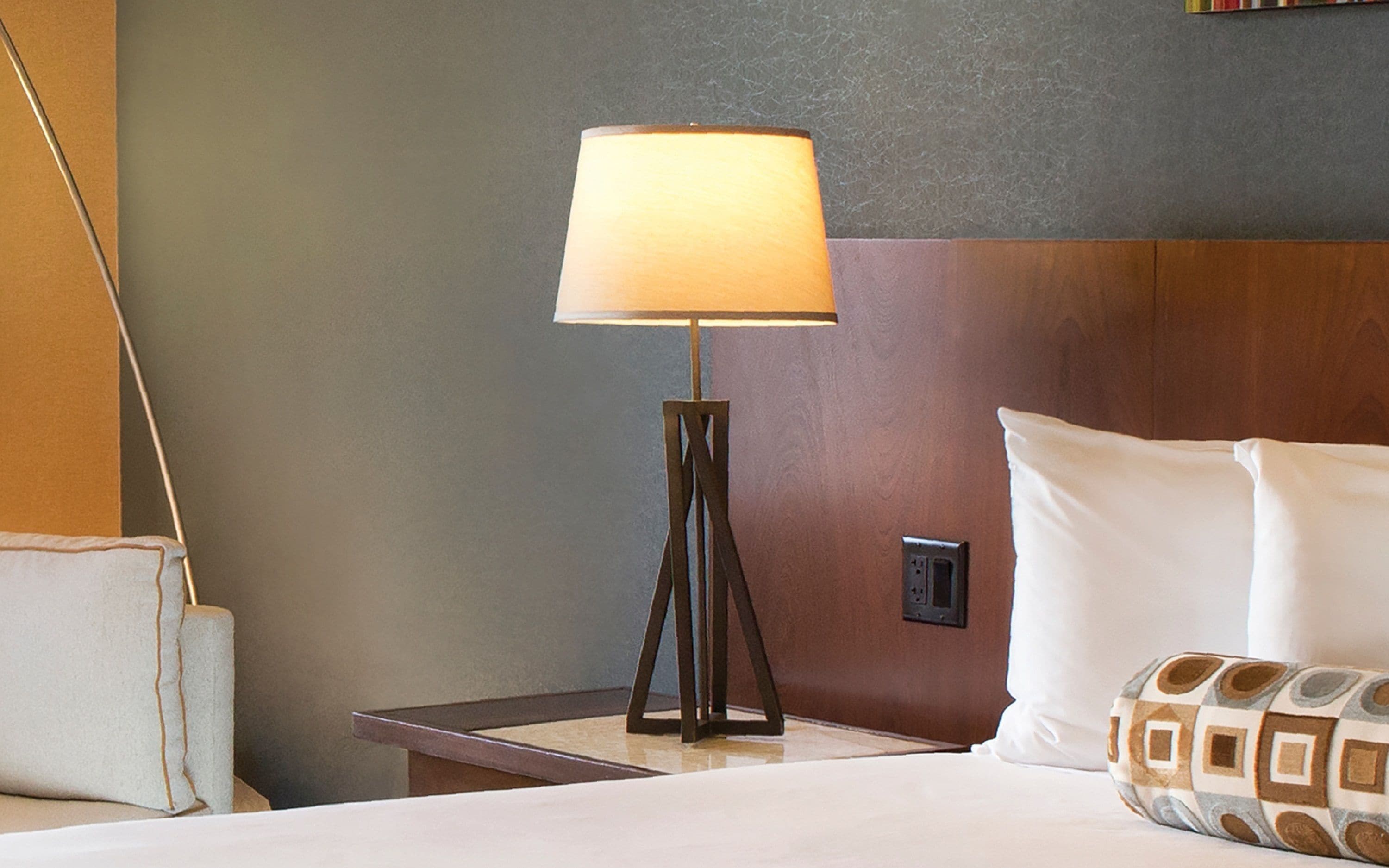 A hotel room with a bedside lamp, a bed with white bedding, and a nightstand.