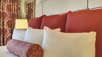 Habitación de hotel con una cama, almohadas rojas y blancas, un cojín decorativo estampado y una lámpara.
