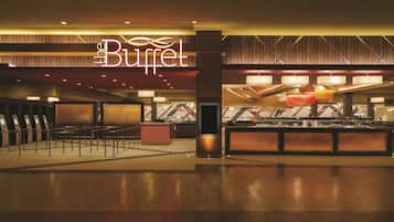 Un hall de hotel con zona de buffet, mostrador de recepción y área de descanso con barandilla.