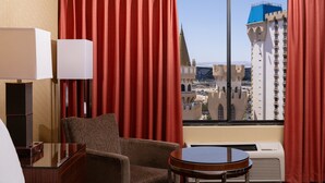 A hotel room with a view of a cityscape, including a tall building with a blue roof.