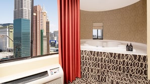 A hotel bathroom with a large window, a bathtub, and a shower area.