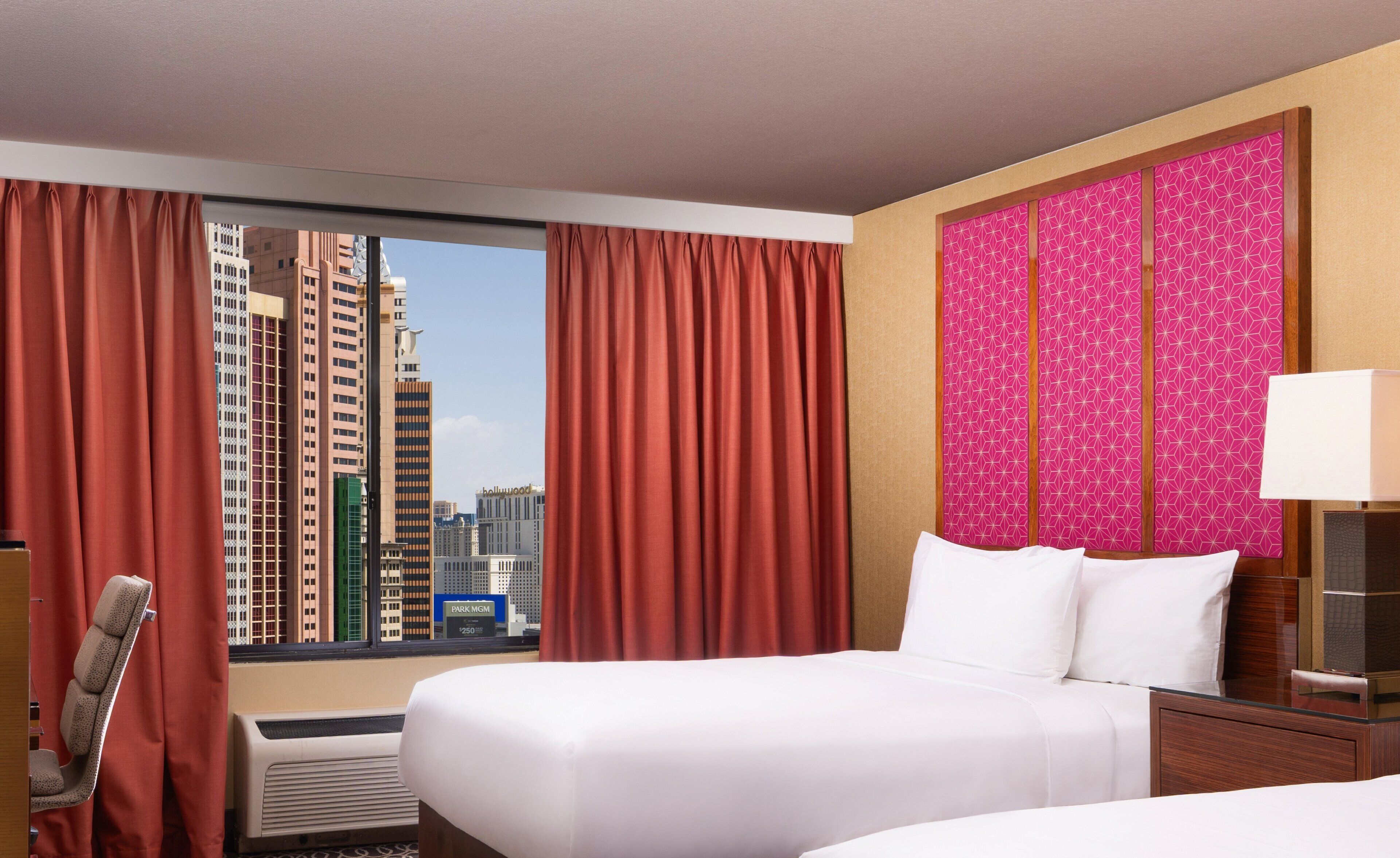 A hotel room with a large bed, a chair, a desk, and a view of tall buildings.