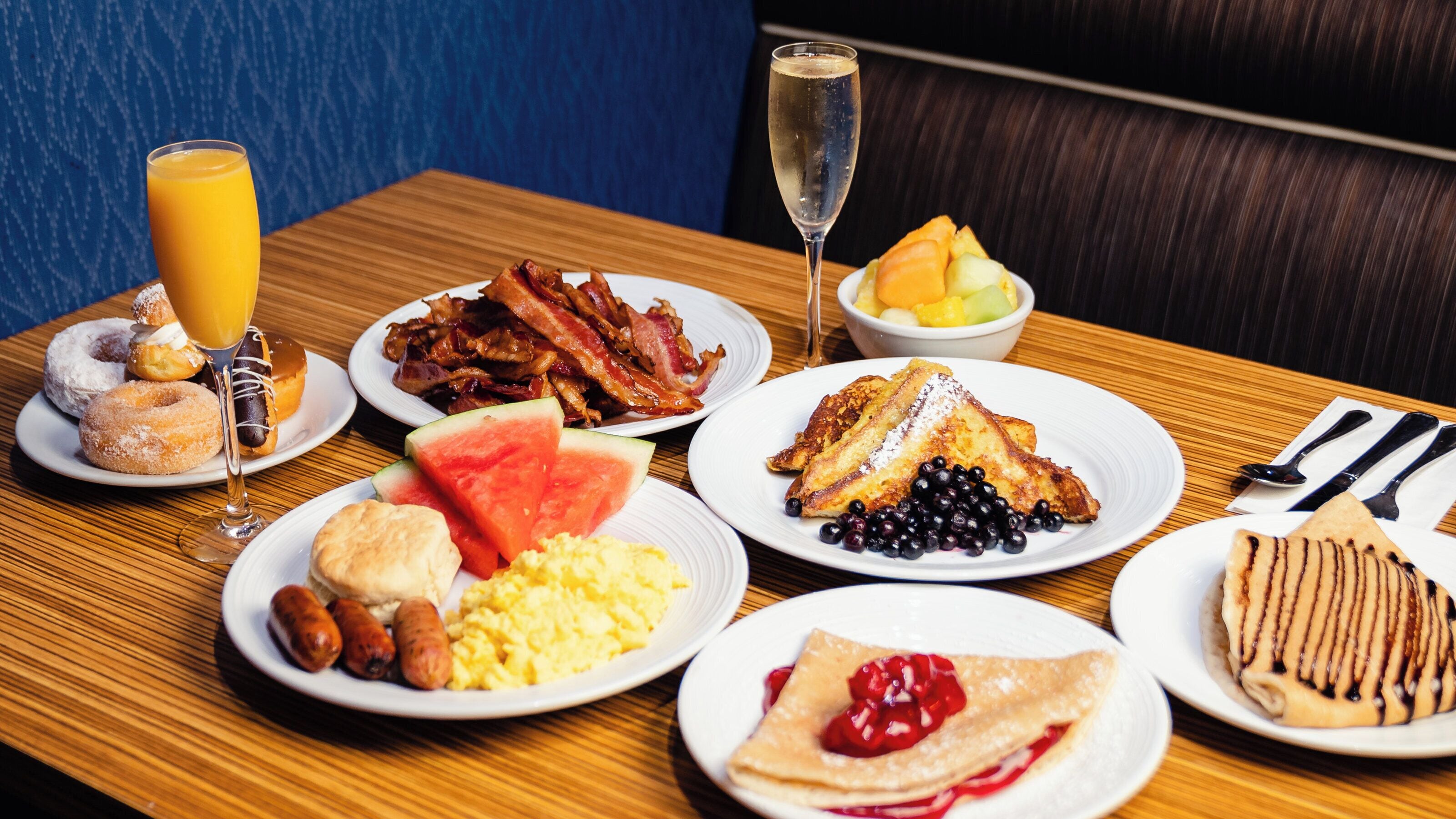 Un buffet de petit-déjeuner proposant divers plats, notamment du bacon, des œufs, des gaufres et un verre de champagne.