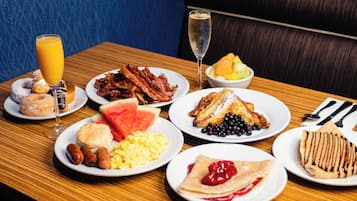 Un buffet de petit-déjeuner proposant divers plats, notamment du bacon, des œufs, des gaufres et un verre de champagne.